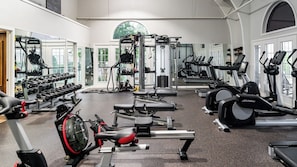 Un gimnasio con varios equipos de ejercicio, incluyendo cintas de correr, elípticas y máquinas de pesas.