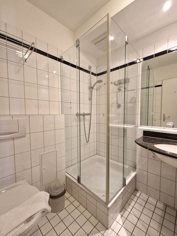 Een moderne badkamer met een douchecabine van glas, een vloer van witte tegels en een zwart aanrechtblad met een wastafel.