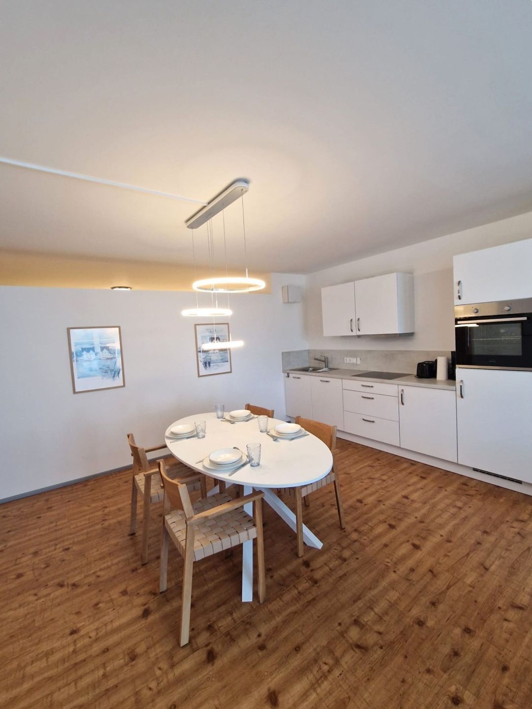 Una cucina moderna con mobili bianchi, forno integrato e zona pranzo con tavolo rotondo e sedie in legno.