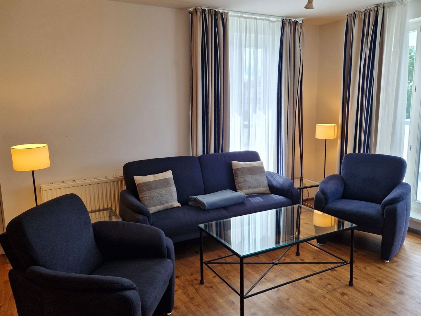 Ein Wohnzimmer mit einer Couch, zwei Sesseln, einem Glastisch und einer Heizung.