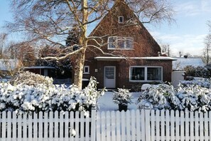 Een bakstenen huis met een witte hekken, omringd door met sneeuw bedekte struiken.