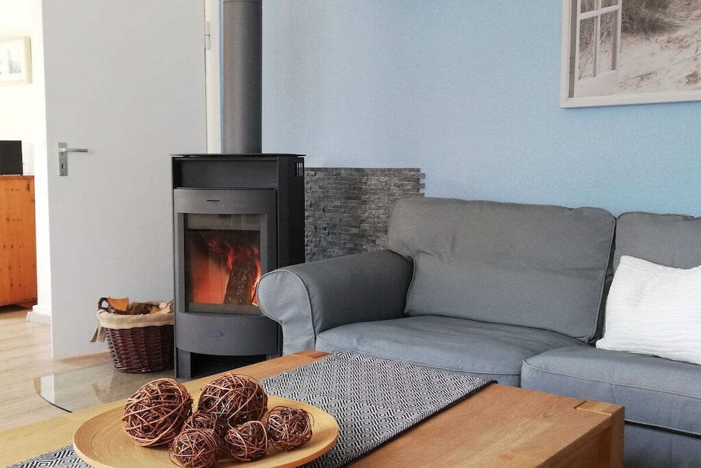 A living room with a grey sofa, a wooden coffee table with decorative balls, a fireplace with visible fire, and a stone wall.