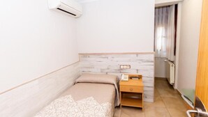 A small, single-bed room with a wooden nightstand, a telephone, and a radiator. - HOSTAL VIKY (Madrid)