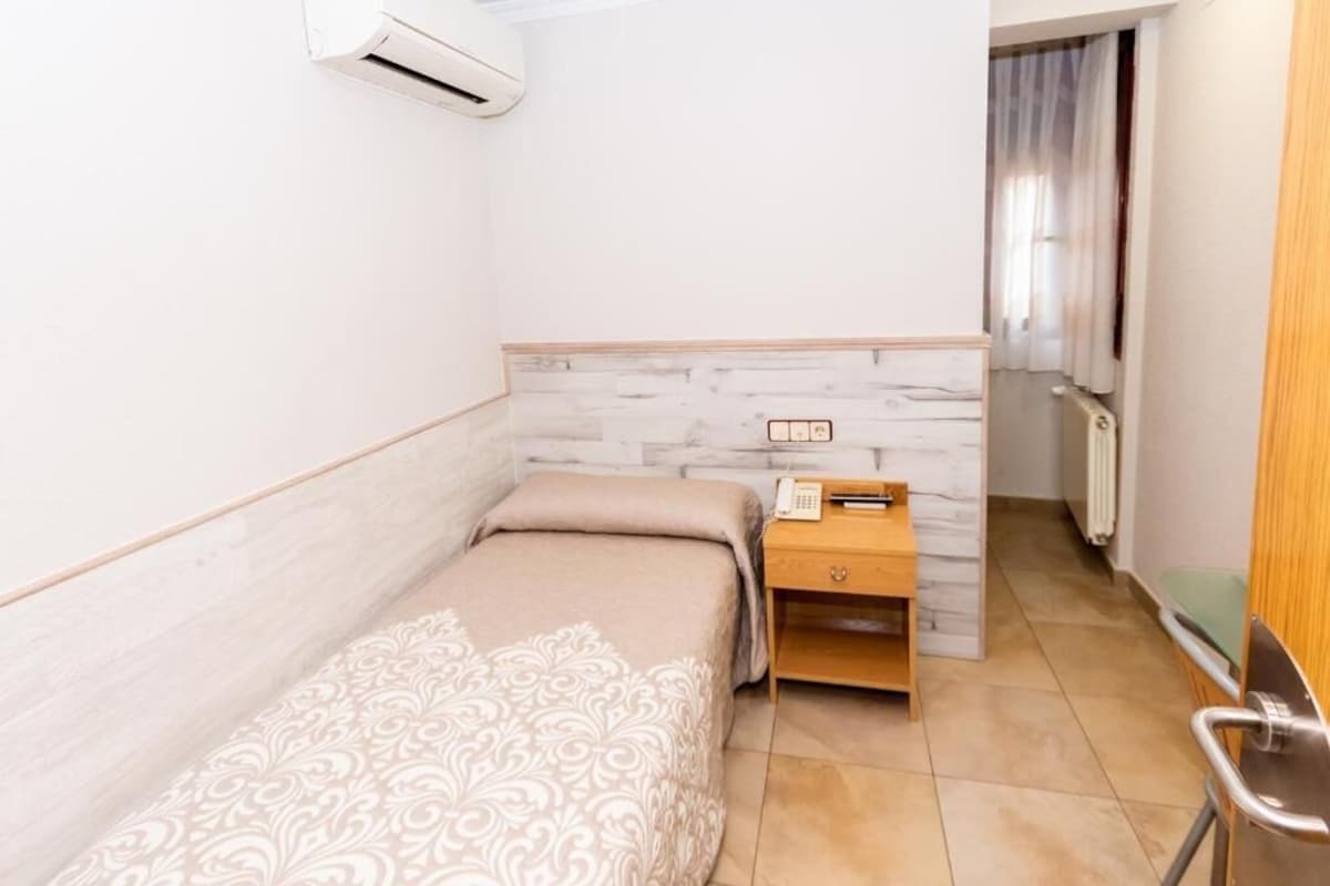 A small, single-bed room with a wooden nightstand, a telephone, and a radiator.