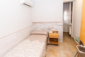 A small, single-bed room with a wooden nightstand, a telephone, and a radiator. - HOSTAL VIKY (Madrid)