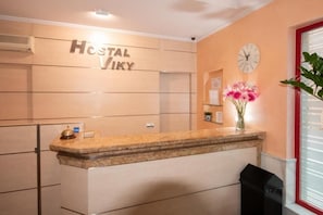 A reception desk with a clock and a vase of flowers. - HOSTAL VIKY (Madrid)