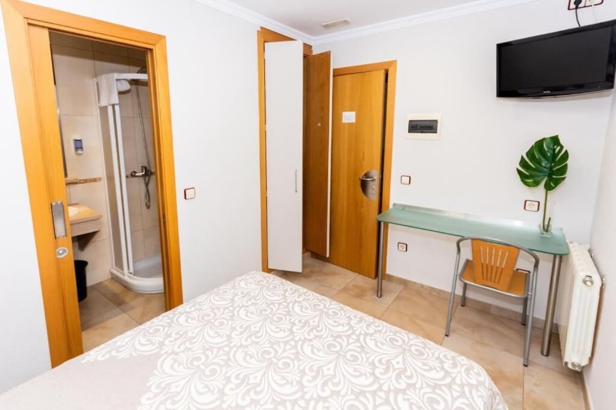 A hotel room with a bed, a desk, a chair, a shower, and a television.