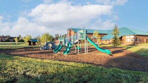Ein Spielplatz mit Rutschen und Klettergerüsten, umgeben von einer Rasenfläche und einem Gebäude mit Gründach.
