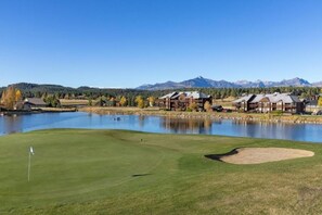 A golf course with a lake, a flag, and buildings in the background.