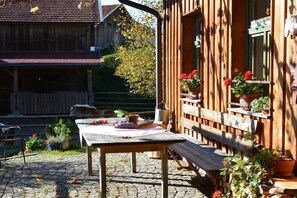 Eine Terrasse aus Holz mit Tisch und Bank, umgeben von Blumentöpfen und einem rustikalen Gebäude.