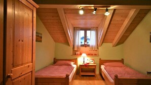 Une pièce avec deux lits en bois, une fenêtre avec des rideaux, une armoire en bois et un plafond avec des poutres en bois.