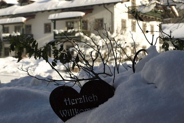 Schneebedeckte Landschaft mit einem herzförmigen Schild, auf dem 'Herzlich Willkommen' steht.