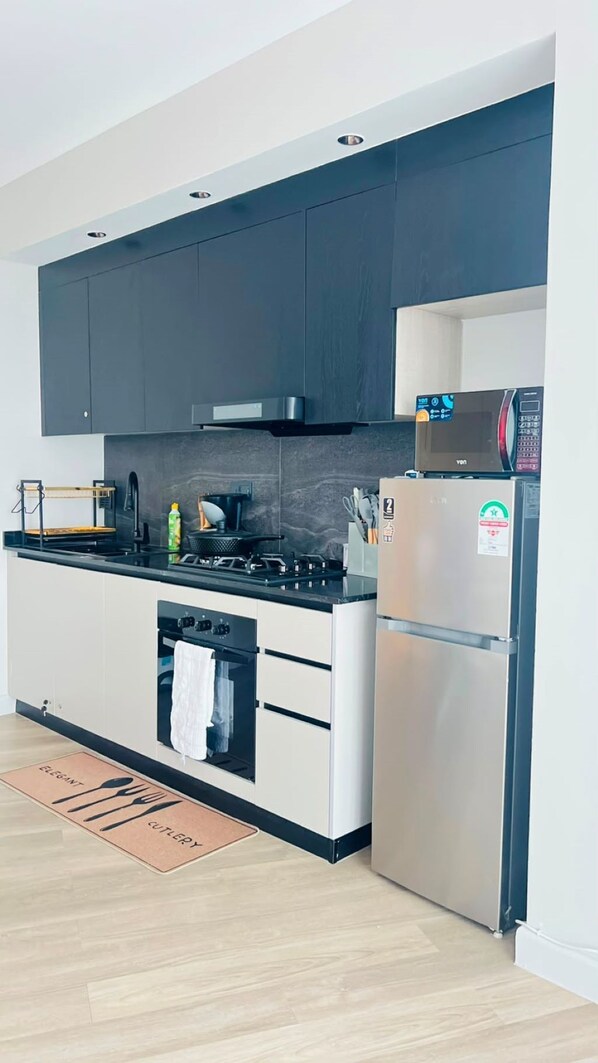 A modern kitchen with dark cabinets, a stainless steel refrigerator, and a built-in oven.