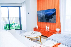 A modern living room with a sofa, a round coffee table, and a flat-screen TV mounted on an orange wall.