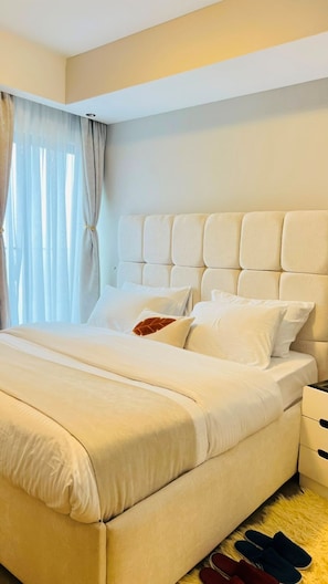 Une chambre d’hôtel avec un grand lit, une tête de lit, une table de chevet et une paire de chaussons posés sur le sol.