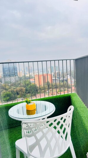 A balcony with a glass table and white plastic chair, overlooking a cityscape. - Altura View Palace- 2 Bedroom (Nairobi)