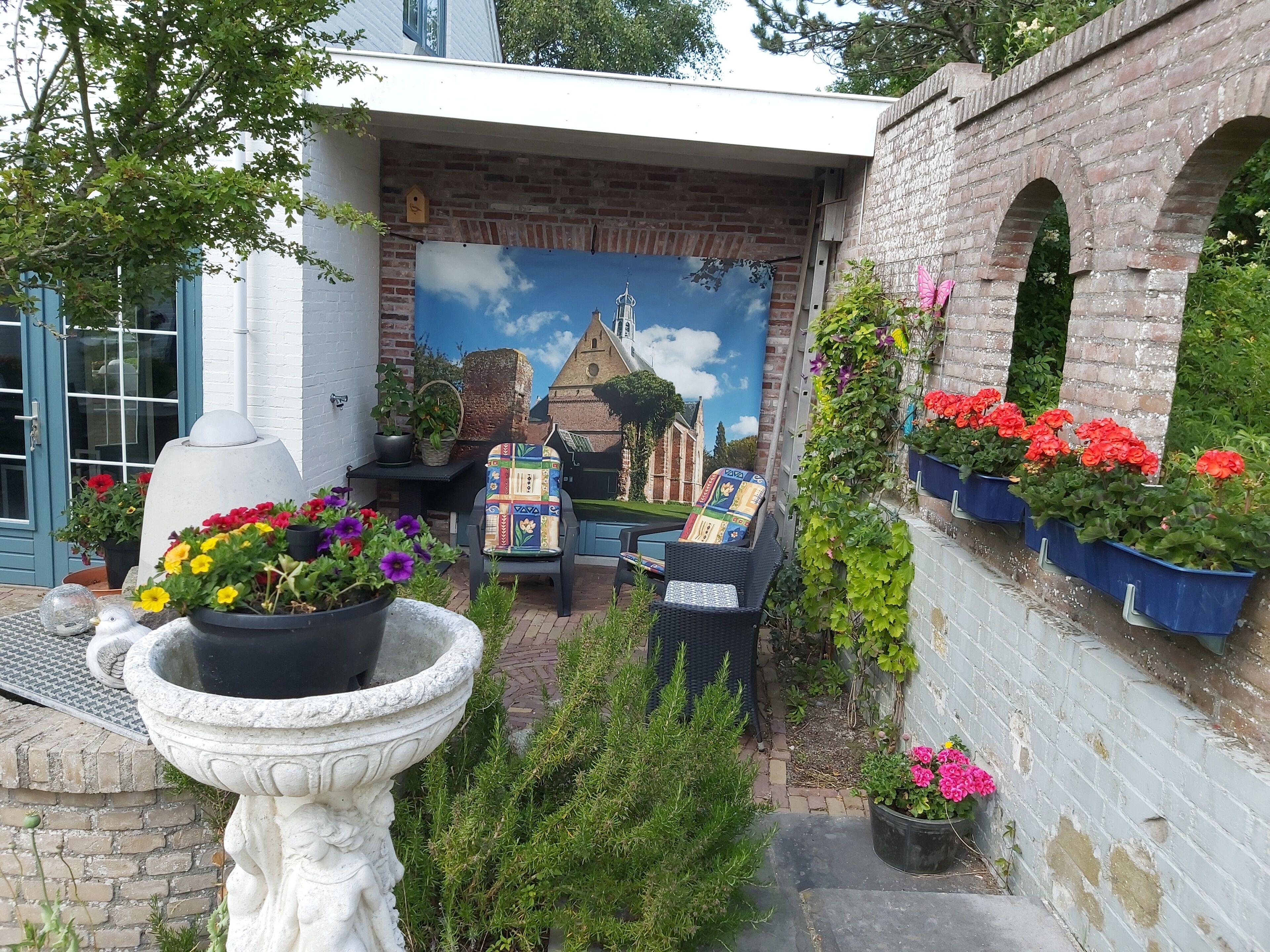Ein Innenhof mit Wandmalerei, Blumentöpfen, einer Sitzgelegenheit und einem Vogelbad aus Stein.