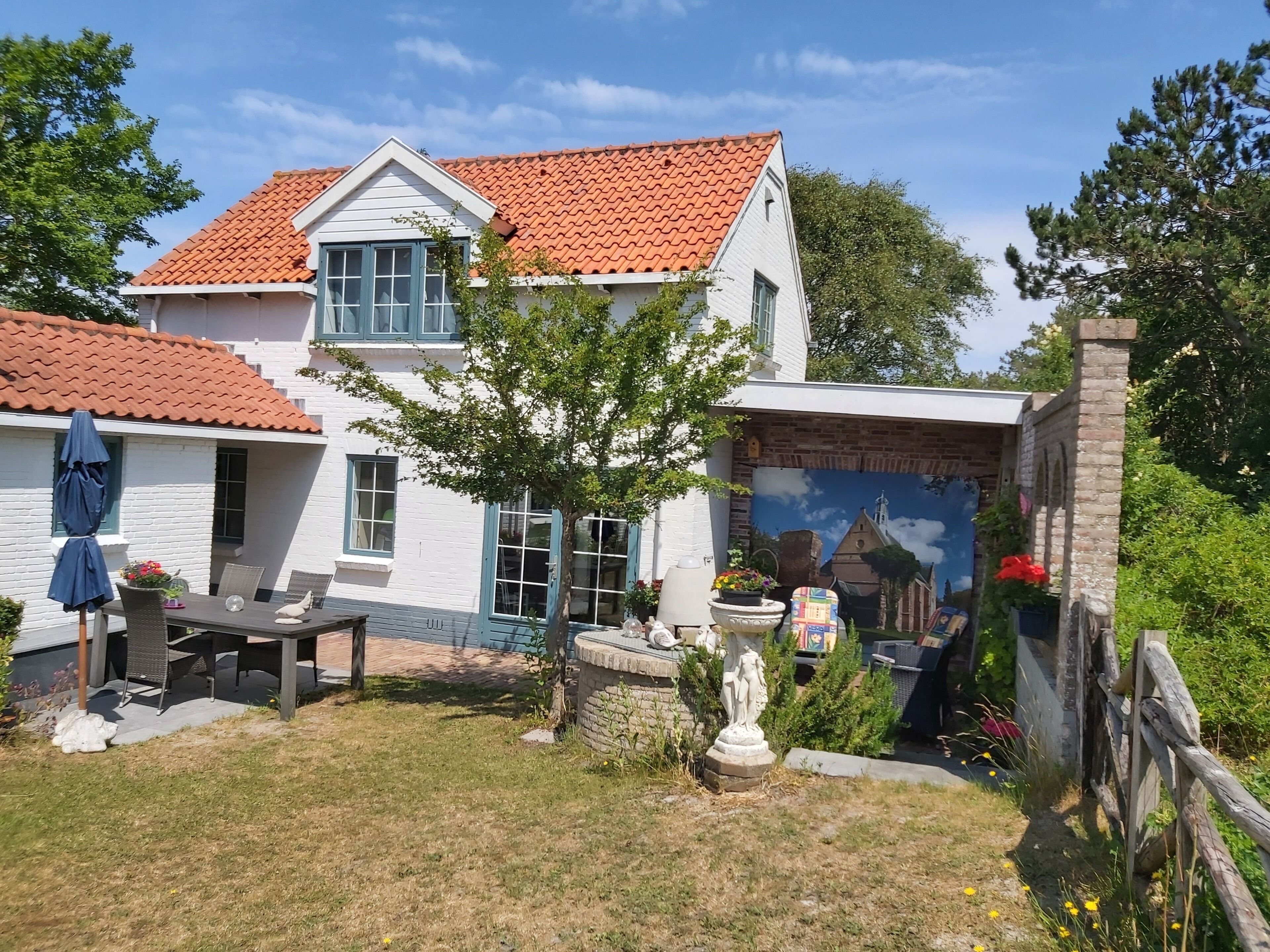 A two-story house with a red-tiled roof, a patio with outdoor furniture, and a mural on the side.