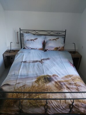 A bed with a metal frame, two bedside tables, and a wall-mounted radiator. - This apartment is located 300 meters from the beach and the sea, right next to the Pettemerbos. (Petten)