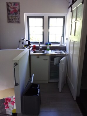 A compact kitchen with a window, a sink, a small refrigerator, and a trash bin. - This apartment is located 300 meters from the beach and the sea, right next to the Pettemerbos. (Petten)