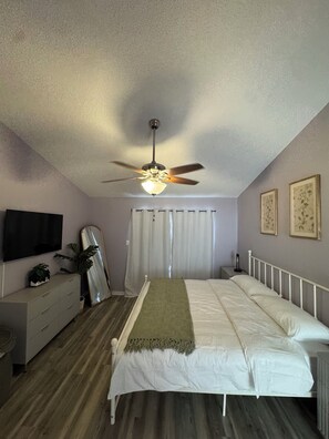 A bedroom with a bed, a ceiling fan, a TV, a dresser, a mirror, and curtains. - Family-Friendly Kissimmee Stay Near Disney (Kissimmee)