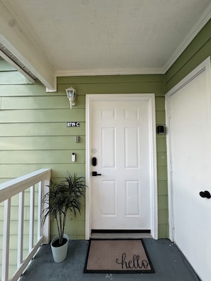 A green house with a white door, a potted plant, and a 'hello' mat. - Family-Friendly Kissimmee Stay Near Disney (Kissimmee)
