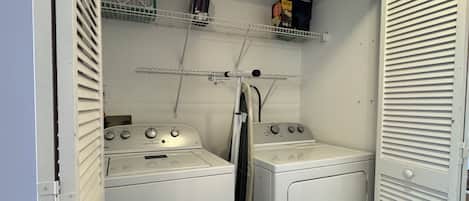 A laundry room with two washers and dryers, a shelf with a box of laundry detergent, and a white door with horizontal slats.