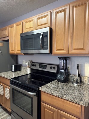 A kitchen with wooden cabinets, a stainless steel microwave, a black stovetop, and a coffee maker. - Family-Friendly Kissimmee Stay Near Disney (Kissimmee)