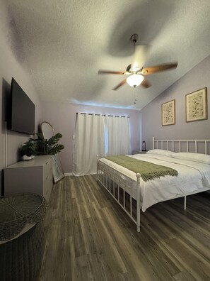 A bedroom with a bed, ceiling fan, curtains, and a flat-screen TV. - Family-Friendly Kissimmee Stay Near Disney (Kissimmee)