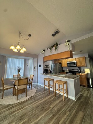 A modern kitchen with wooden cabinets, a central island, and a dining area with a round table and chairs. - Family-Friendly Kissimmee Stay Near Disney (Kissimmee)