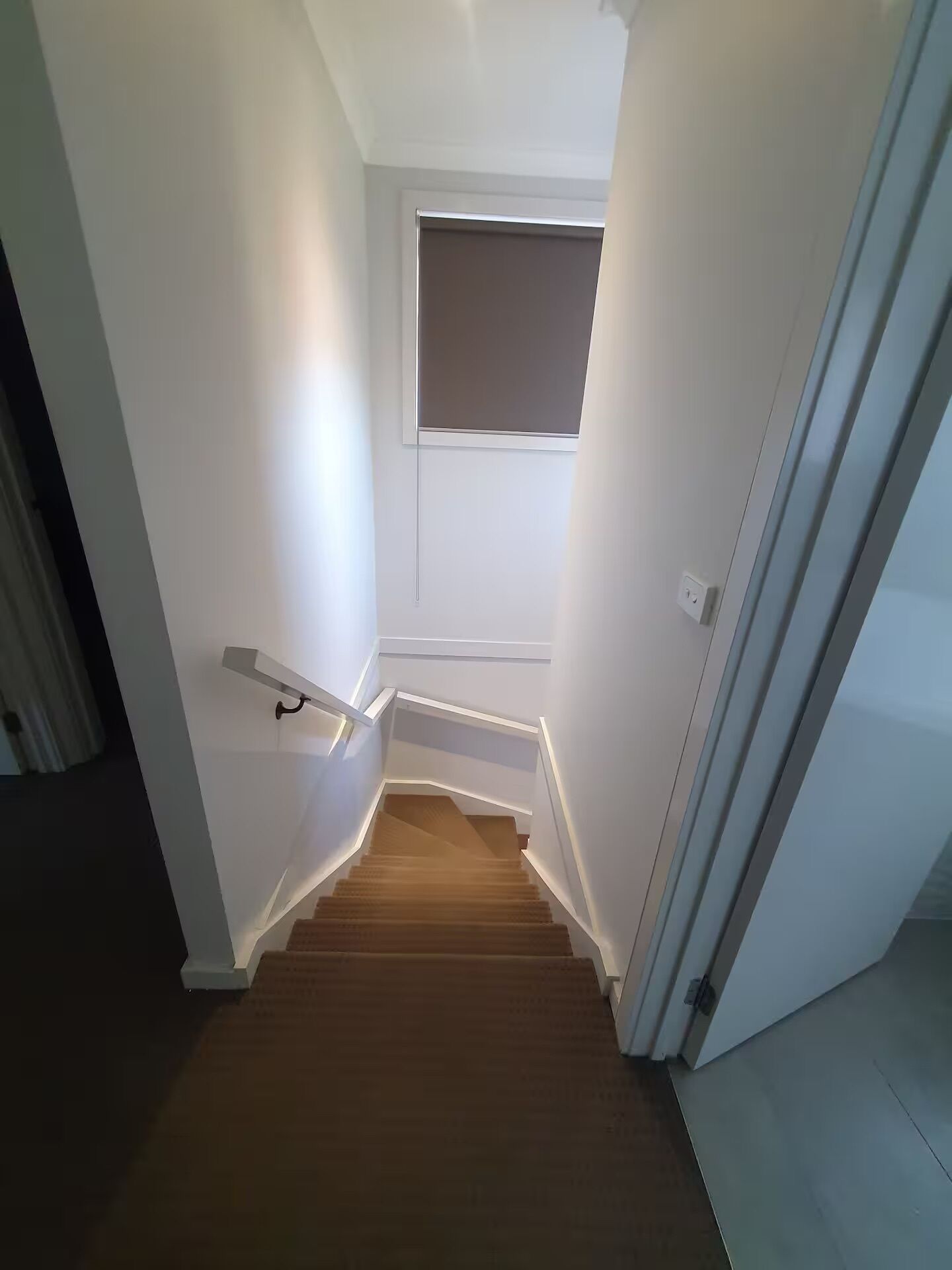 Una escalera estrecha con barandilla, que lleva a un rellano con un pequeño ventanal.