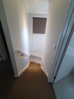 Un escalier étroit doté d’une main courante, menant à un palier avec une petite fenêtre.