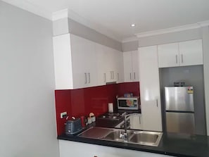 Una cocina moderna con armarios blancos, salpicadero rojo, electrodomésticos de acero inoxidable y encimera negra.