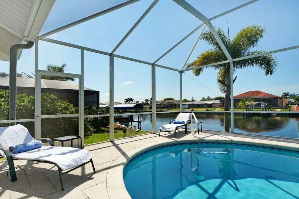 Ein Pool im Freien mit Liegestühlen und Blick auf ein Gewässer und Palmen.