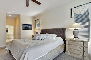 Ein Schlafzimmer mit einem großen Bett, einem Nachttisch mit Lampe, einem Deckenventilator und einem Fenster mit Jalousien.