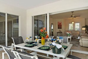 A dining area with a table set for four, a sofa, and a ceiling fan in the background. - CCVS - Villa Blue Bayou (Cape Coral)