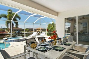 Comedor con una mesa preparada para cuatro, con vista a una piscina y un paisaje de palmeras y agua.