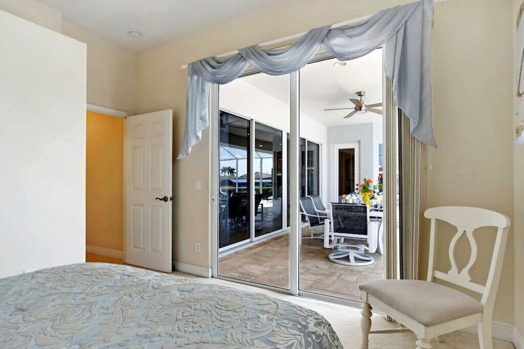 A bedroom with a bed, a chair, a sliding glass door leading to a balcony, and a ceiling fan.