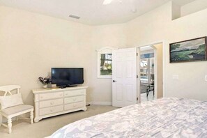 Une chambre à coucher comprenant un lit, une commode, un téléviseur et une porte donnant sur une autre pièce.