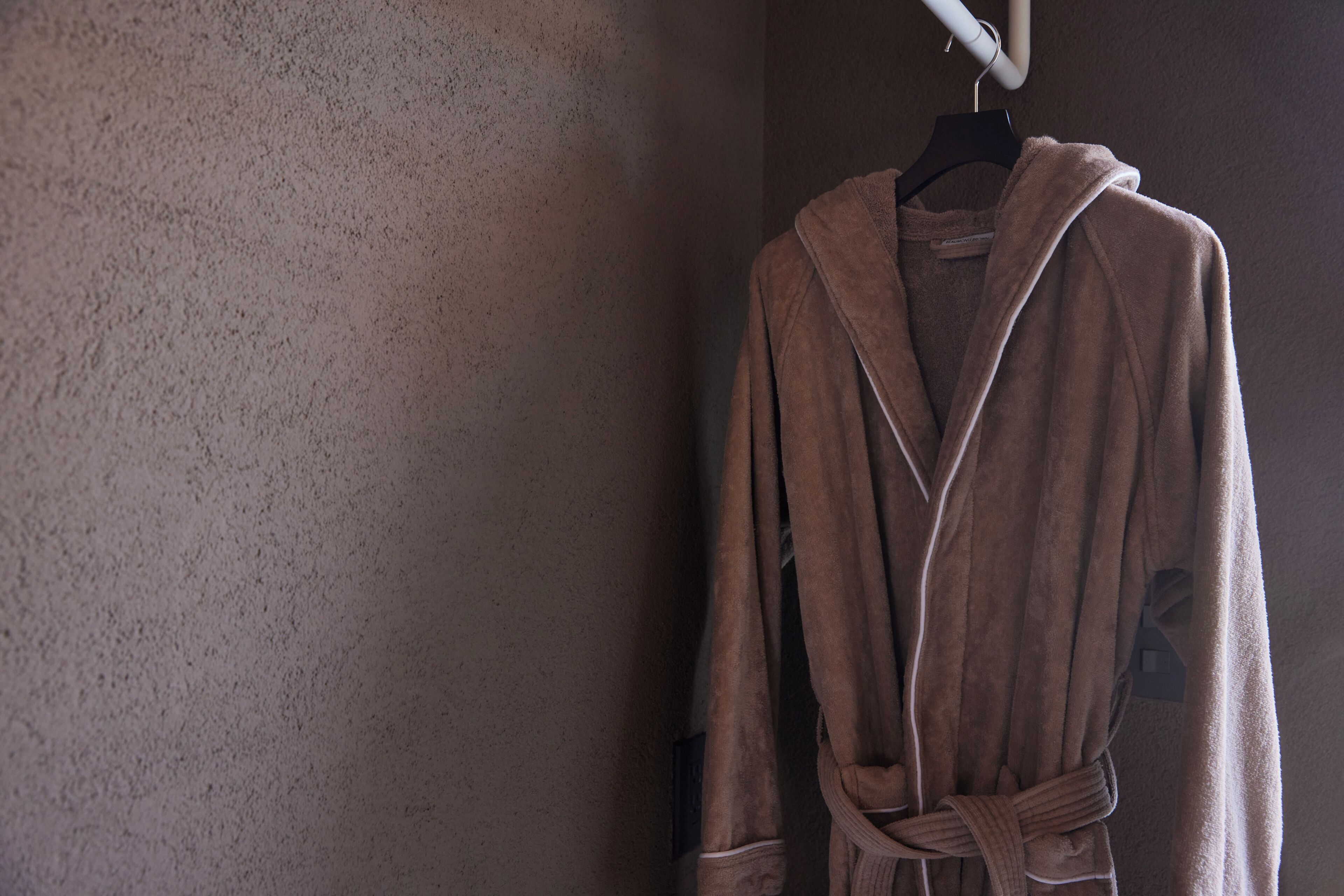 A brown robe hanging on a black hanger against a textured wall.