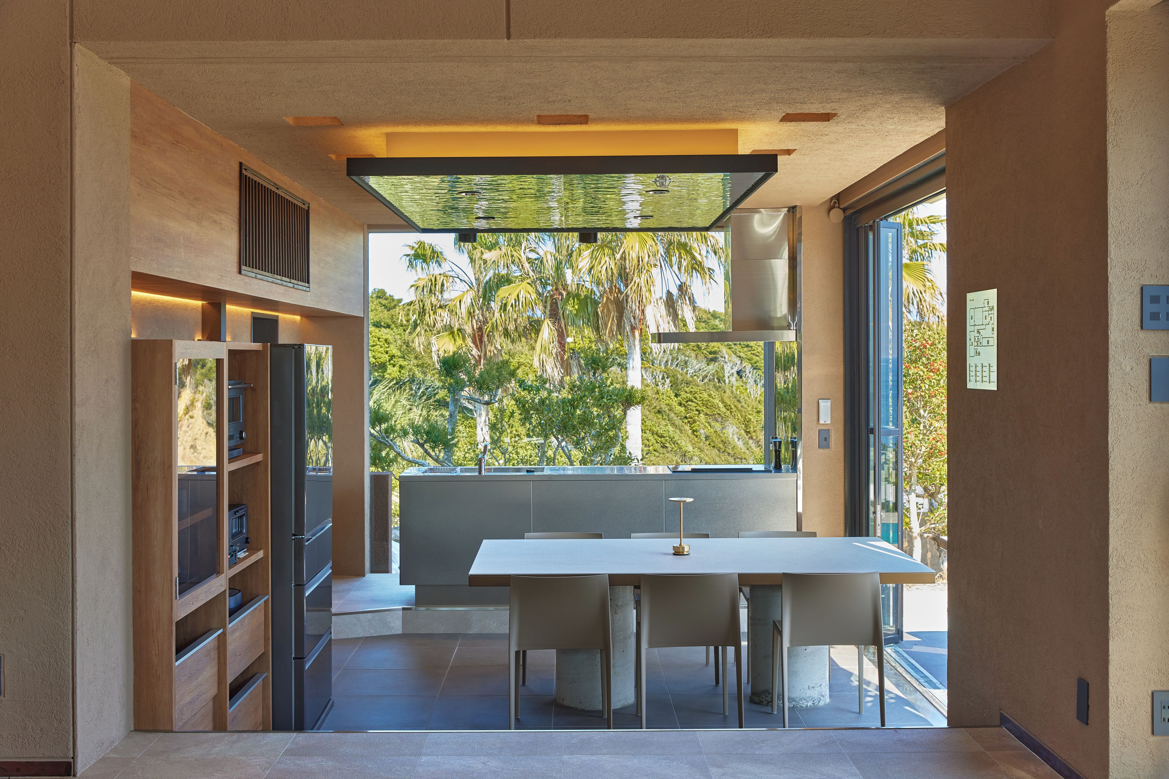 A modern interior with a dining area, built-in shelving, and a view of palm trees.