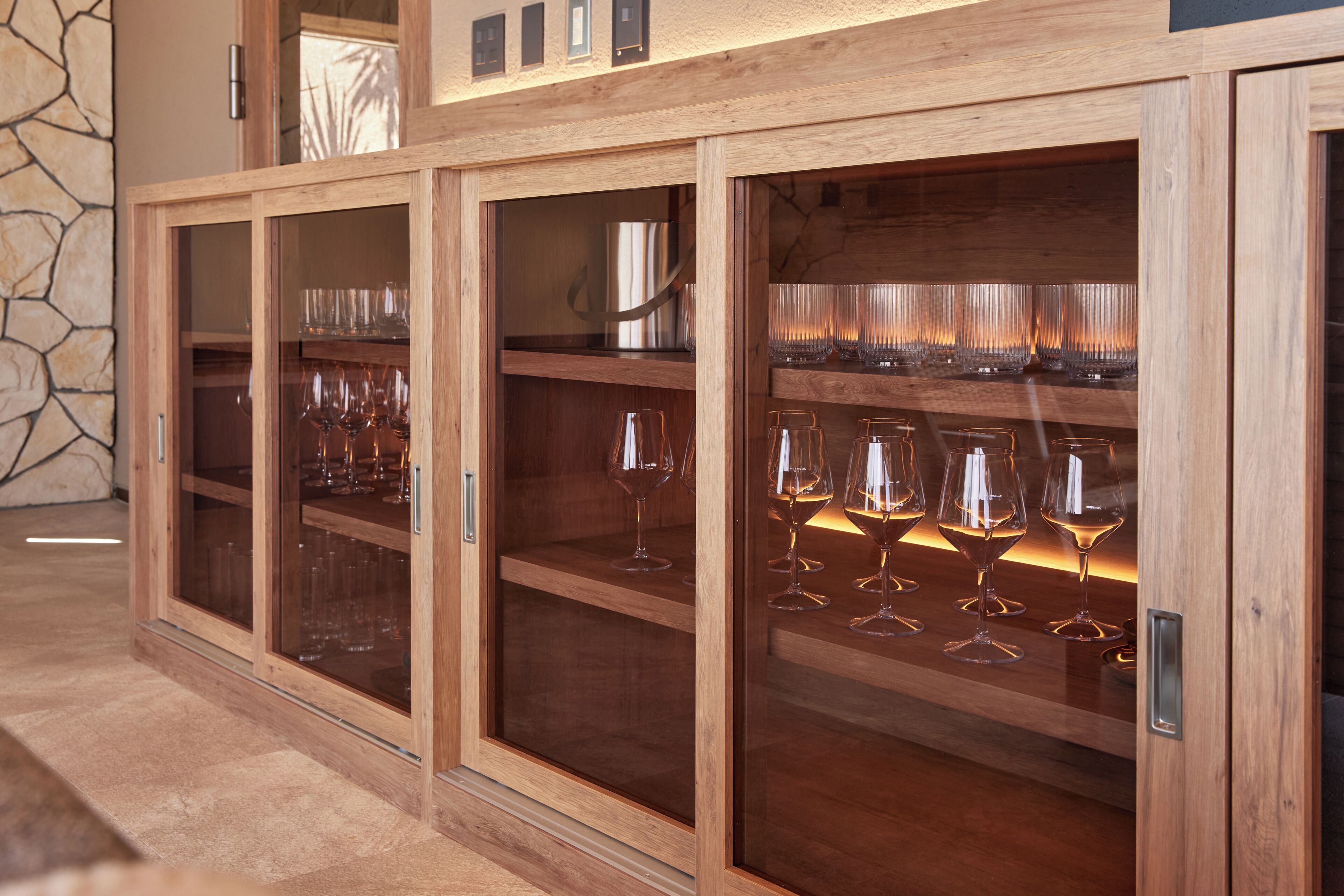 A wooden wine cabinet with multiple shelves, some containing wine glasses.