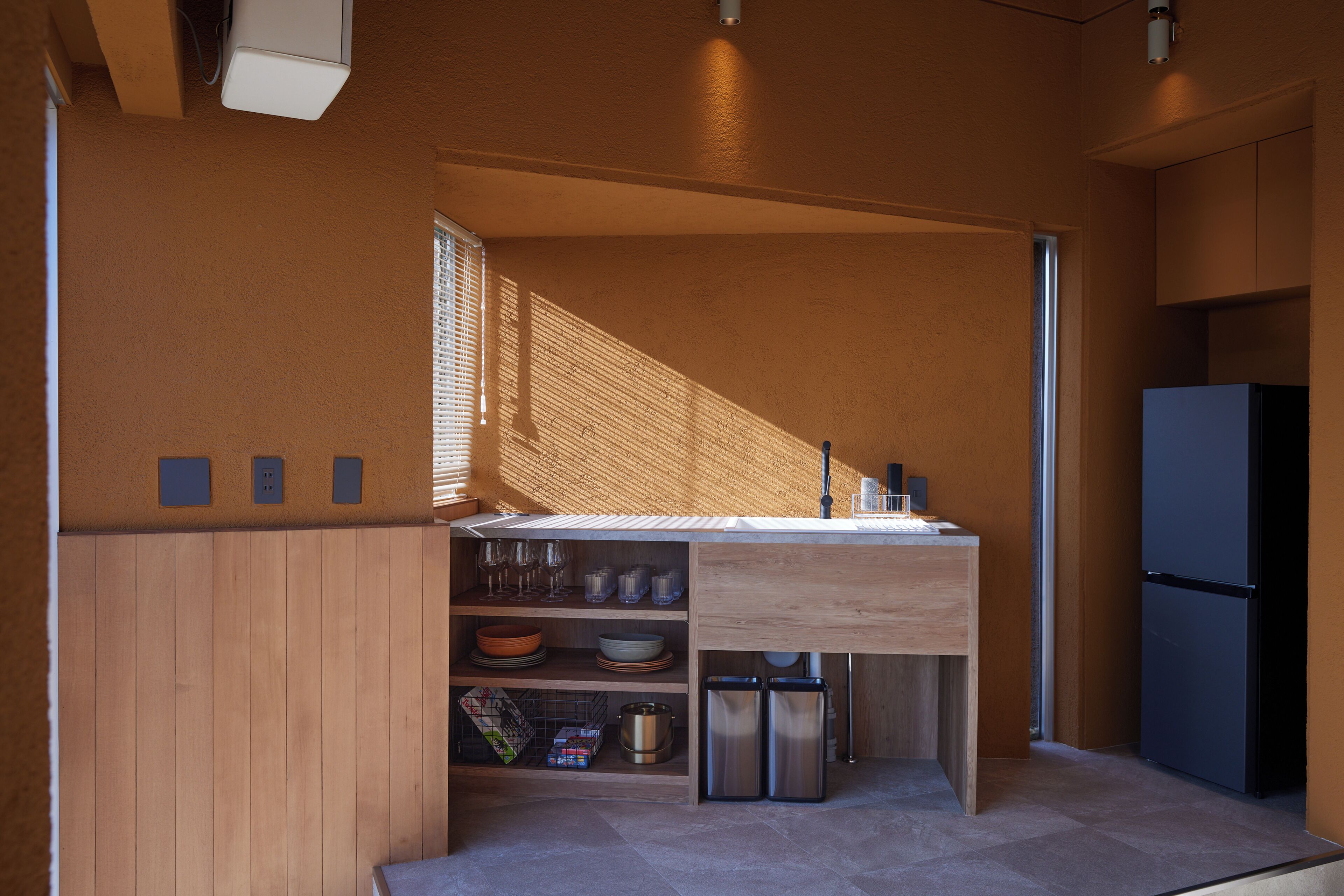 Cocina compacta con lavamanos integrado, muebles de madera y refrigerador de acero inoxidable.