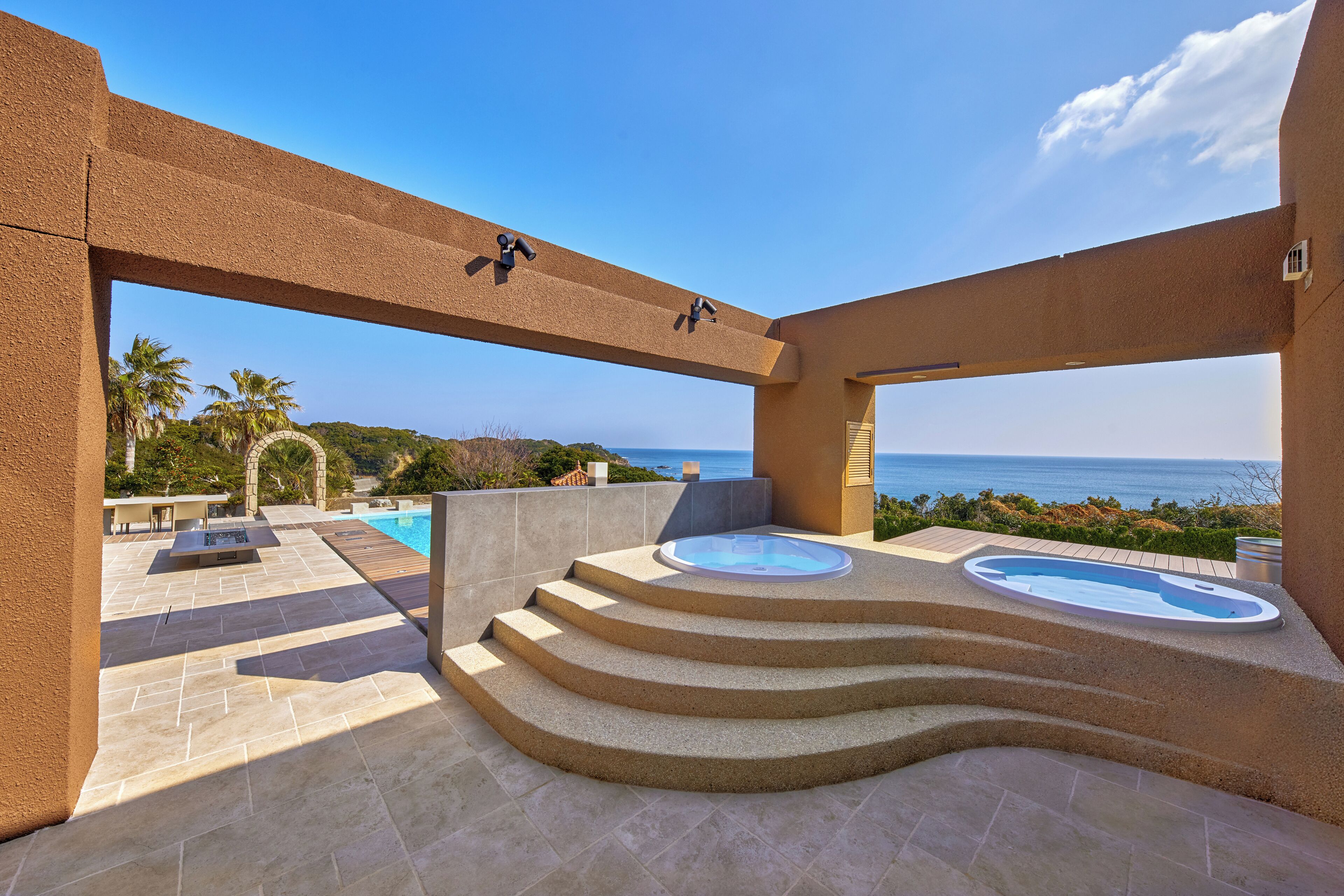 Área de piscina ao ar livre luxuosa, com vista para o mar, uma banheira de hidromassagem e um espaço de estar.