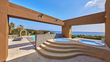 Área de piscina ao ar livre luxuosa, com vista para o mar, uma banheira de hidromassagem e um espaço de estar.