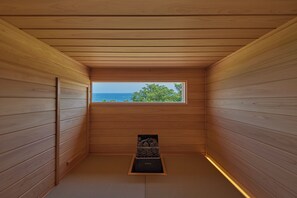 A narrow wooden room with a window overlooking a body of water and greenery.