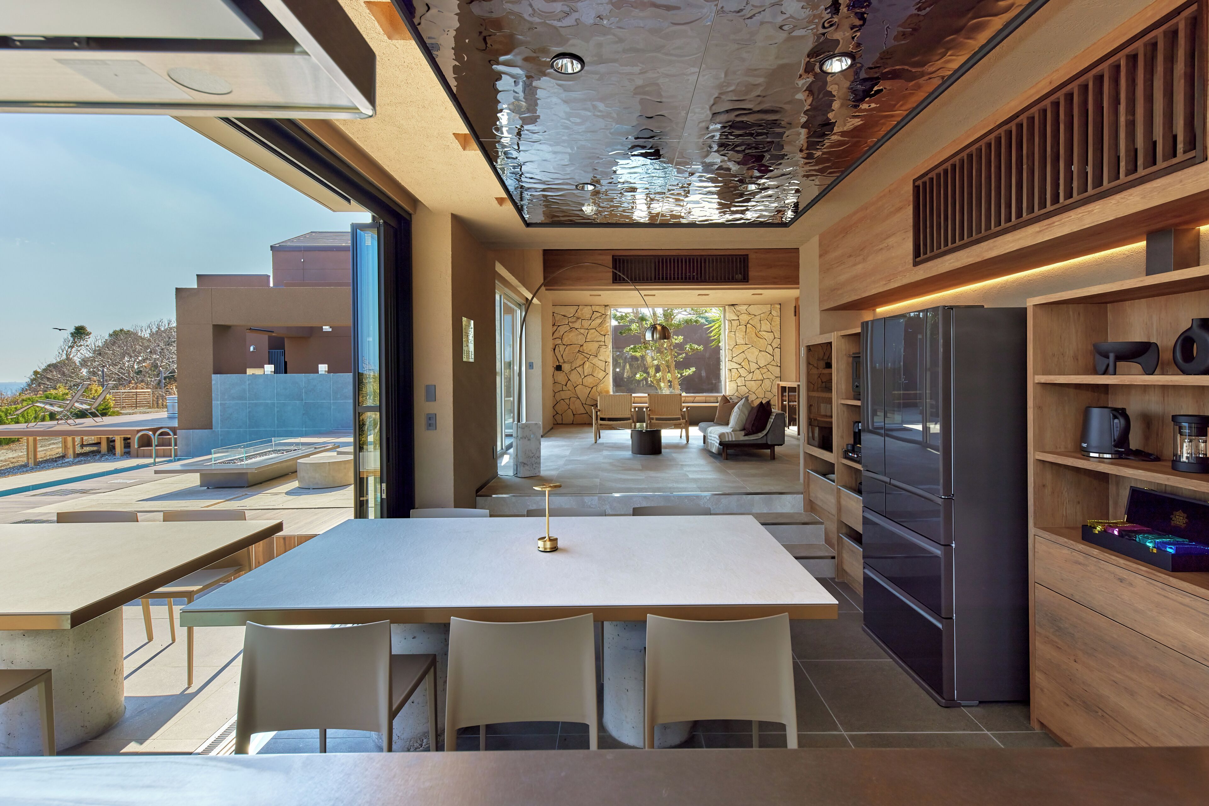 A modern kitchen with a large refrigerator, dining area with chairs, and a view of the outdoors.