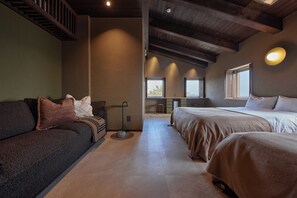 A room with a sofa, two beds, a small table, and a staircase.