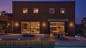 Un edificio moderno de dos pisos con piscina, puertas de cristal y zona de comedor.
