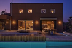 Un edificio moderno de dos pisos con piscina, puertas de cristal y zona de comedor.